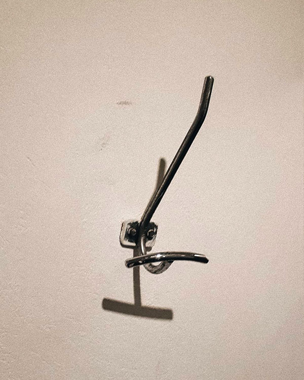 A double hook made of metal, chrome, screwed to a wall. Found on a private home in Mexico City, Mexico, 2020.