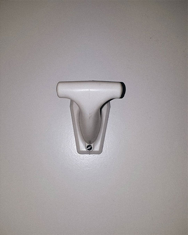 A single hook made of white plastic, screwed to a door. Found on a private home in Val-d'Isère, France, 2020.