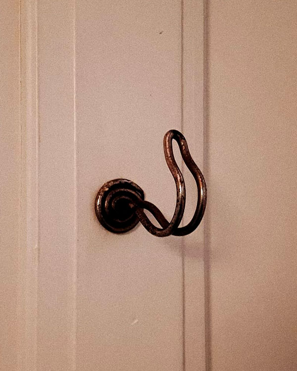 A single hook made of metal, nickel, screwed to a wall. Found on a private home in Apt, France, 2021.