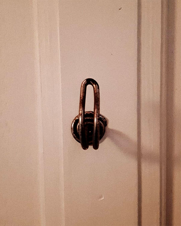 A single hook made of metal, nickel, screwed to a wall. Found on a private home in Apt, France, 2021.