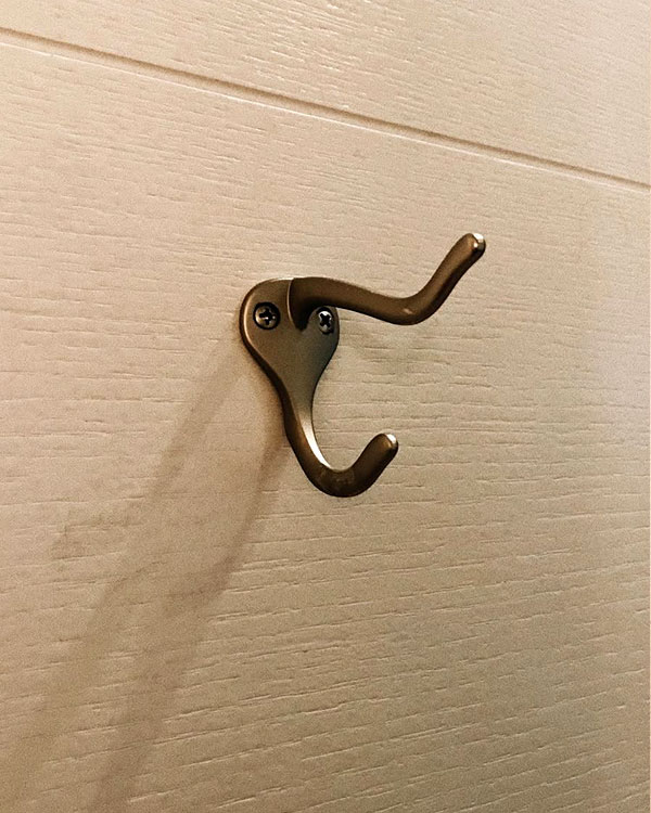 A double hook made of metal, brass, screwed to a door. Found on a private home in New York, USA, 2022.