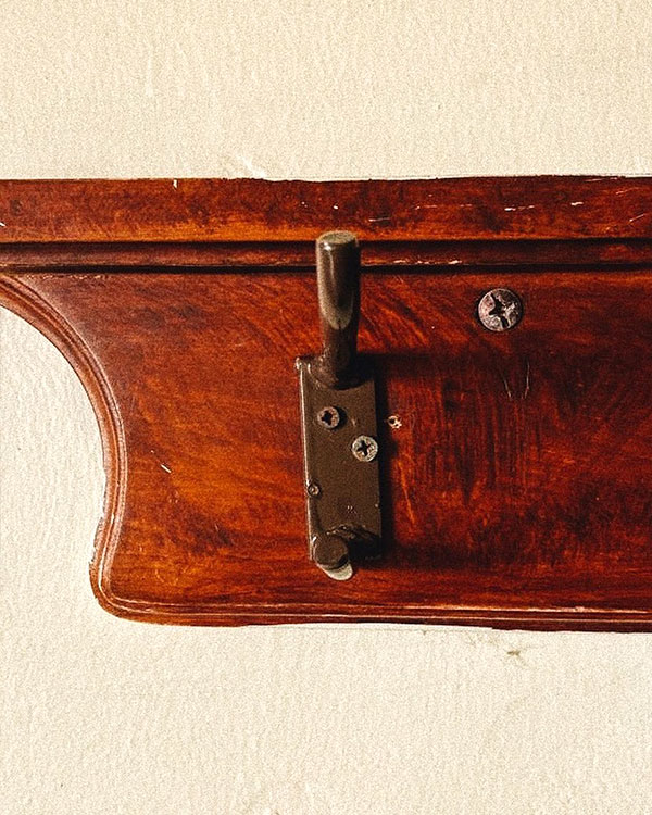 A double hook made of metal, brown paint, screwed to a piece of wood then to a wall. Found on a Spa in Aguascalientes, Mexico, 2022.