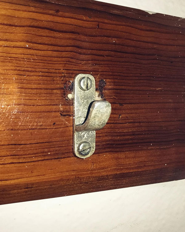 A single hook made of metal, brass, screwed to a piece of wood then to a wall. Found on a Sport Club in Mexico City, Mexico, 2022.