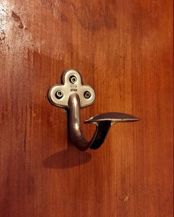 A single hook made of metal, brass, screwed to a door. Found on a restaurant in Barcelona, Spain, 2022.