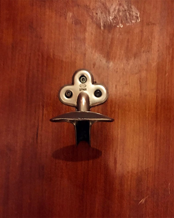 A single hook made of metal, brass, screwed to a door. Found on a restaurant in Barcelona, Spain, 2022.