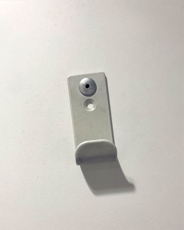 A single hook made of white plastic, riveted to a door. Found on a public bathroom in Avignon, France, 2022.