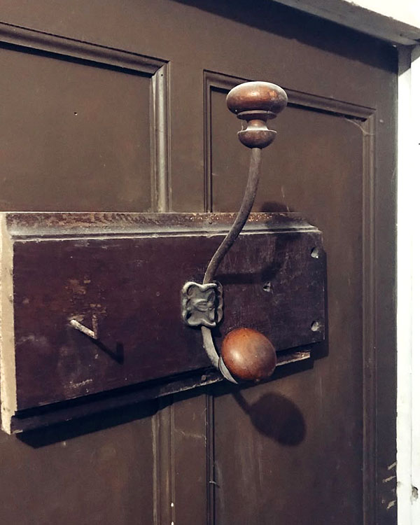 A double hook made of metal and wood, oxide, screwed to a piece of wood then to a door. Found on a private home in Apt, France, 2022.