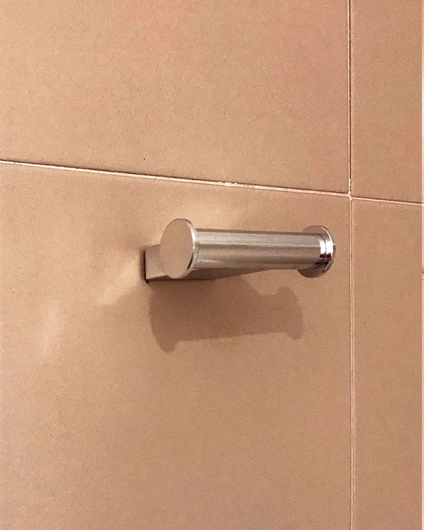 A double hook made of metal, chrome, fixed to a wall. Found on a hotel in Roses, Spain, 2022.