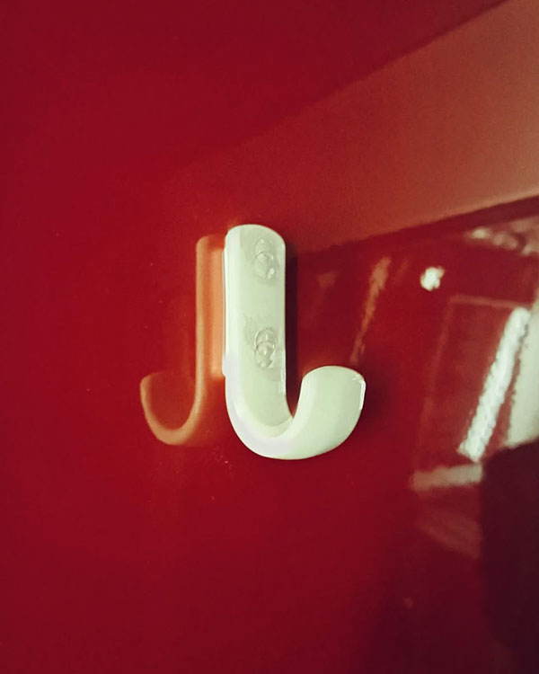 A single hook made of ivory plastic, screwed to a wall. Found on a train near Amsterdam, Netherlands, 2023.