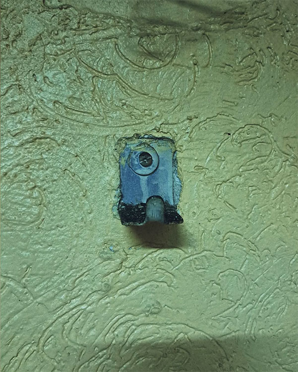 A single hook made of metal, gray paint, screwed to a wall. Found on a restaurant in Mexico City, Mexico, 2023.