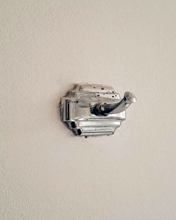A single hook made of metal, chrome, fixed to a wall. Found on a private home in Mexico City, Mexico, 2023.