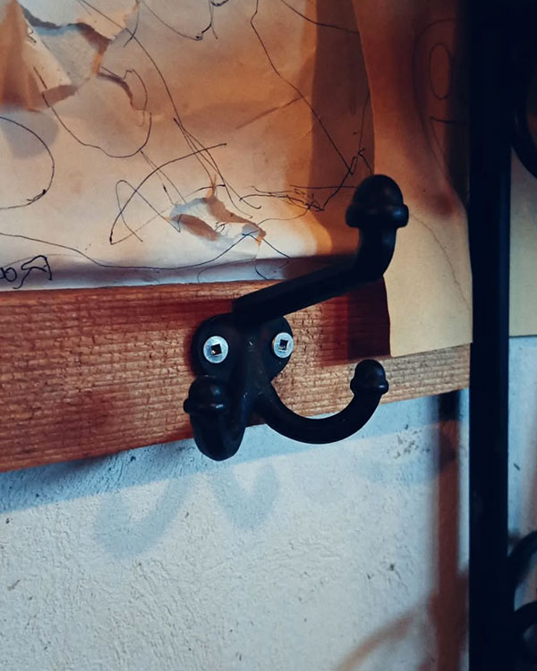 A triple hook made of metal, black paint, screwed to a wall. Found on a private home in Montreal, Canada, 2024.