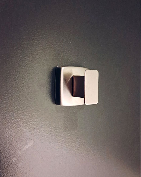 A single hook made of metal, nickel, fixed to a door. Found on a museum in Montreal, Canada, 2024.