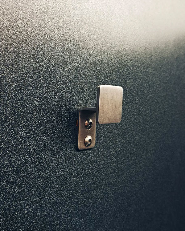 A single hook made of metal, nickel, riveted to a door. Found on an airport in Montreal, Canada, 2024.