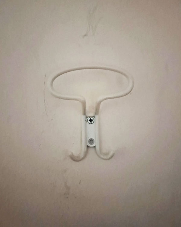 A triple hook made of metal, white powder, screwed to a wall. Found on a hotel in Pietra Ligure, Italy, 2024.