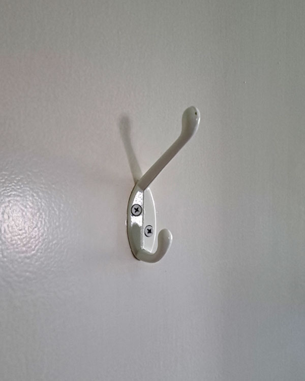 A double hook made of metal, white powder, screwed to a door. Found on a private home near NY, USA, 2025.