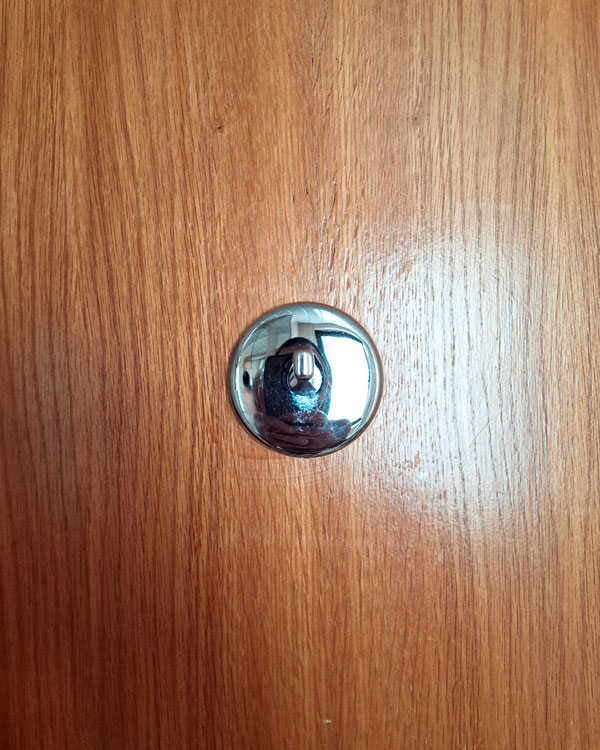 A single hook made of metal, chrome, fixed to a door. Found on a hotel in Porto, Portugal, 2025.
