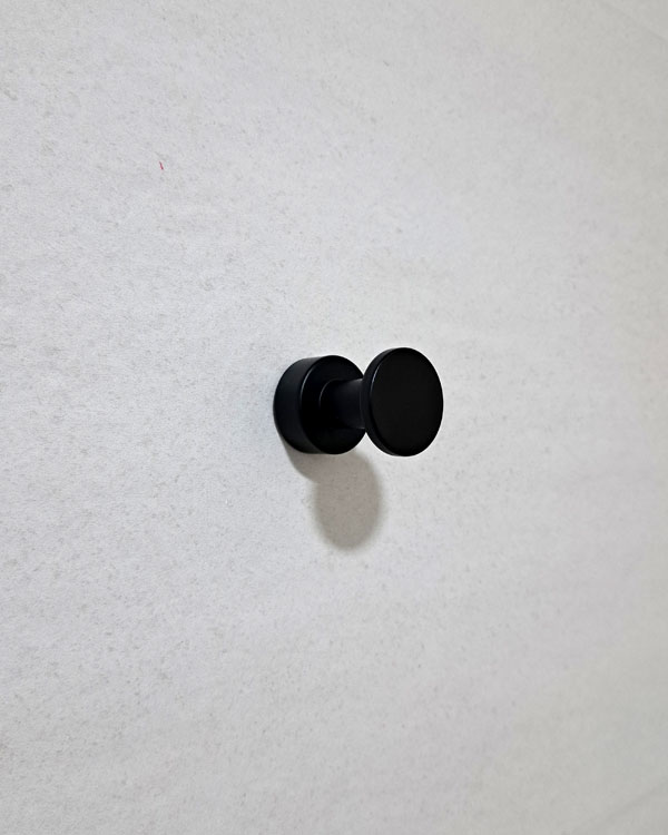 A single hook made of metal, black powder, fixed to a wall. Found on a museum in Porto, Portugal, 2025.