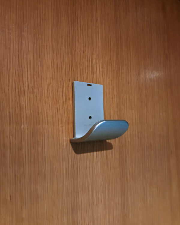 A single hook made of metal, nickel, screwed to a door. Found on a restaurant in Barcelona, Spain, 2025.