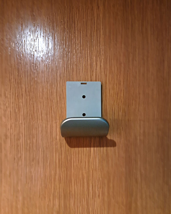 A single hook made of metal, nickel, screwed to a door. Found on a restaurant in Barcelona, Spain, 2025.