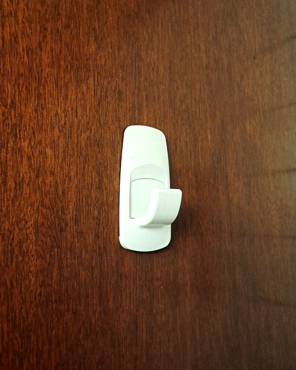 A single hook made of white plastic, glued to a door. Found on a home in Mexico City, Mexico, 2025.