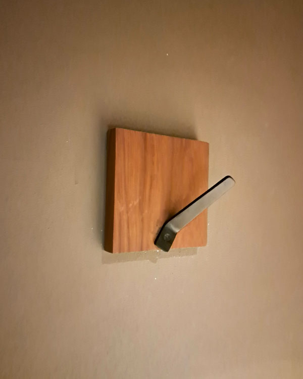 A single hook made of metal, nickel, screwed to a piece of wood then to a wall. Found on a restaurant in Mexico City, Mexico, 2025.