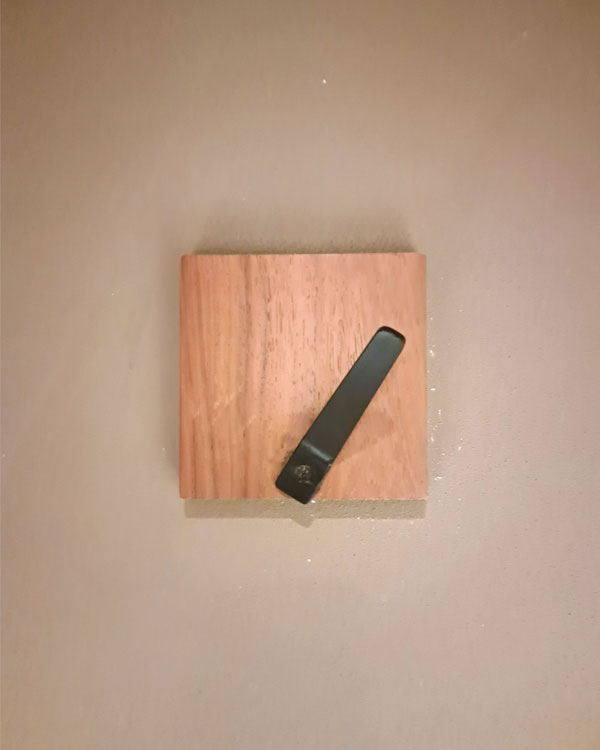 A single hook made of metal, nickel, screwed to a piece of wood then to a wall. Found on a restaurant in Mexico City, Mexico, 2025.