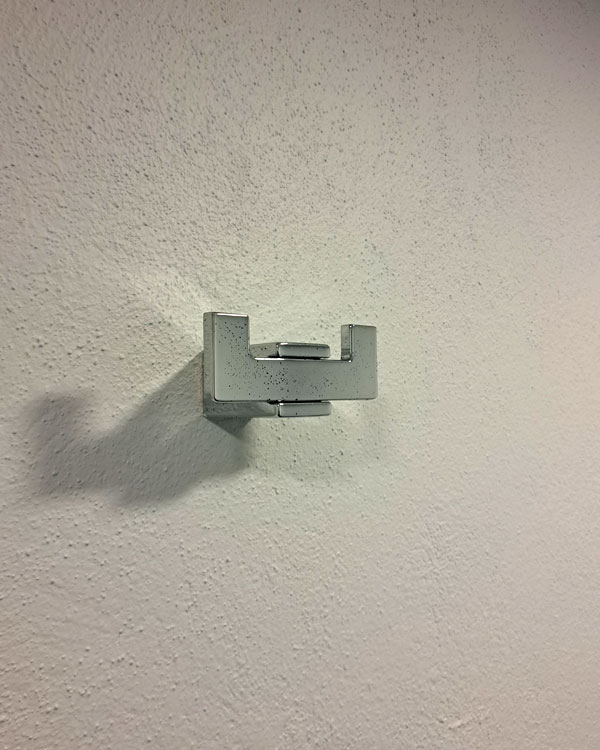 A double hook made of metal, chrome, fixed to a wall. Found on a funeral home in Mexico City, Mexico, 2026.